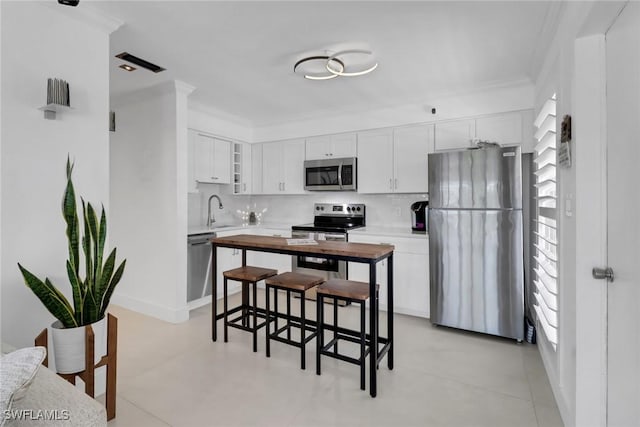 kitchen with a healthy amount of sunlight, white cabinetry, ornamental molding, and appliances with stainless steel finishes