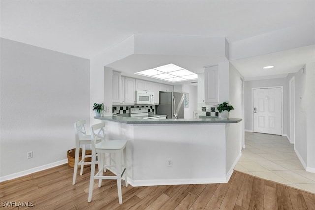 kitchen with white appliances, light hardwood / wood-style floors, kitchen peninsula, and white cabinets