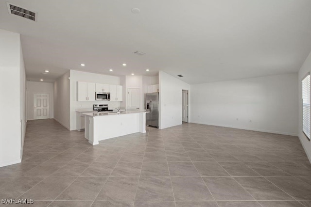 kitchen featuring appliances with stainless steel finishes, light tile patterned floors, a center island with sink, and white cabinetry