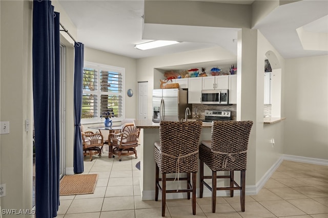 kitchen featuring a breakfast bar area, light tile patterned floors, tasteful backsplash, appliances with stainless steel finishes, and a peninsula