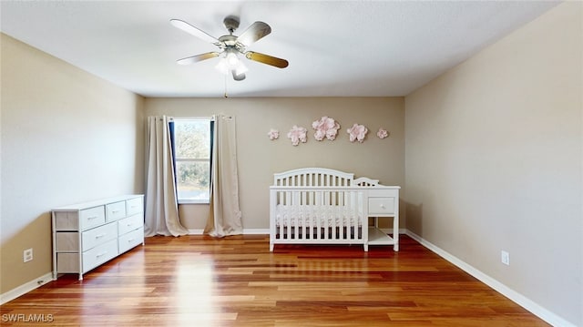 unfurnished bedroom with wood-type flooring, a nursery area, and ceiling fan