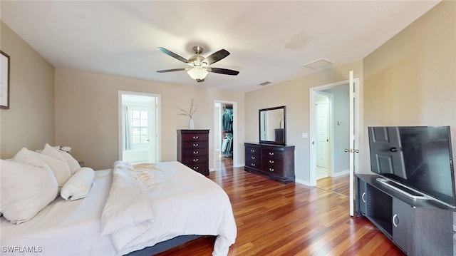 bedroom with ceiling fan, a walk in closet, dark wood-type flooring, and a closet