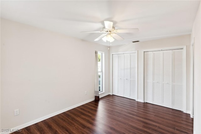 unfurnished bedroom featuring baseboards, visible vents, a ceiling fan, dark wood-style floors, and multiple closets