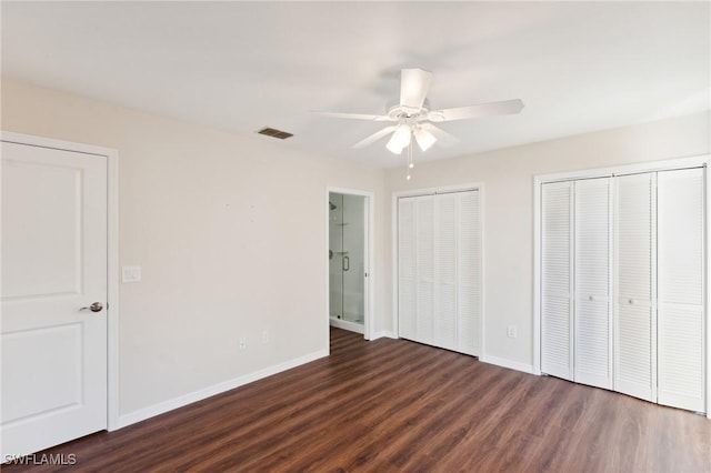 unfurnished bedroom with visible vents, dark wood finished floors, baseboards, and two closets