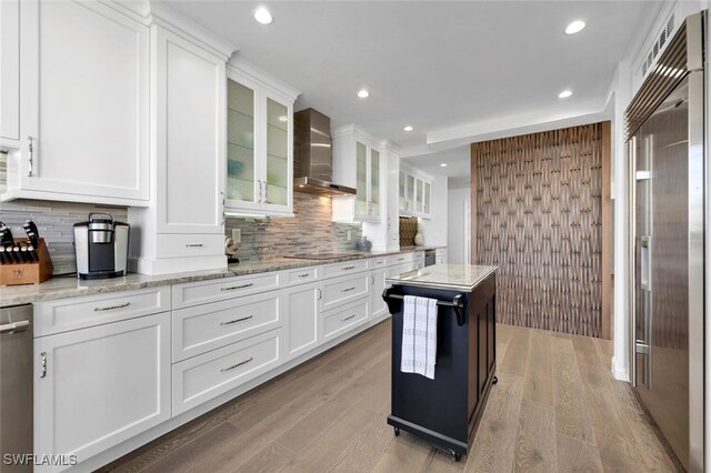 kitchen featuring stainless steel appliances, white cabinetry, wall chimney exhaust hood, and light stone counters