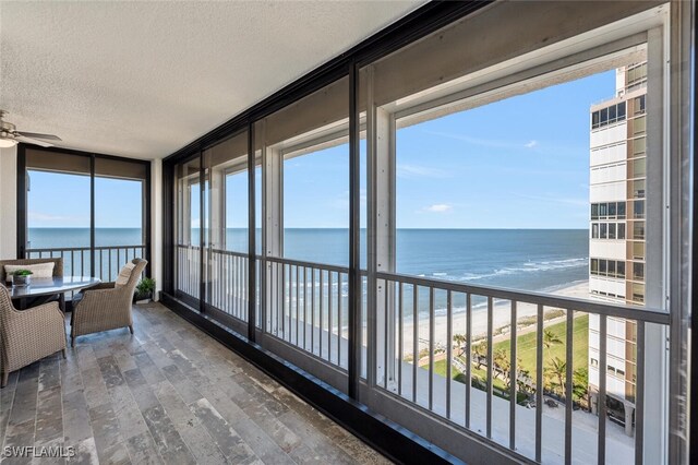 sunroom with a view of the beach, a water view, ceiling fan, and a healthy amount of sunlight