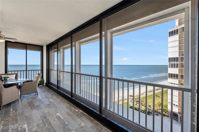 sunroom / solarium featuring a healthy amount of sunlight, a ceiling fan, and a water view