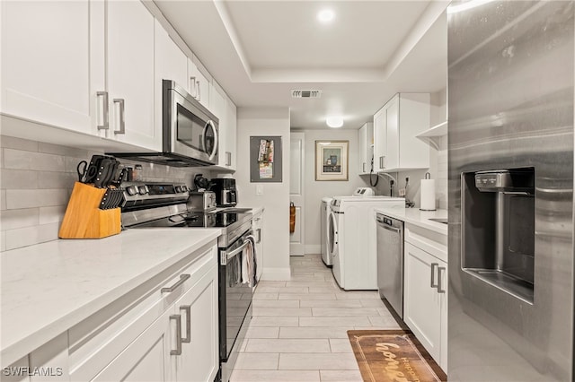 kitchen with stainless steel appliances, separate washer and dryer, light stone counters, backsplash, and white cabinets