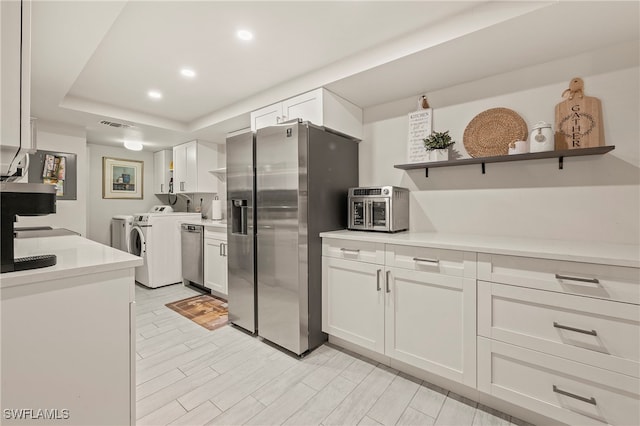 kitchen featuring a raised ceiling, white cabinetry, washer and dryer, and appliances with stainless steel finishes