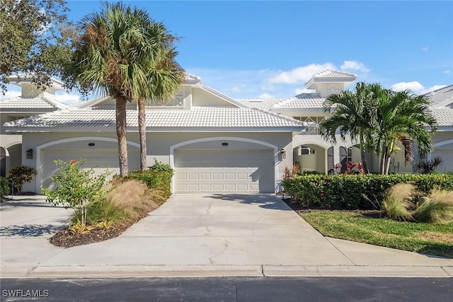 mediterranean / spanish-style home with a tile roof, stucco siding, concrete driveway, and a garage