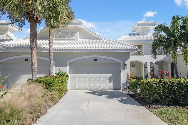 mediterranean / spanish house with a tile roof, concrete driveway, a garage, and stucco siding