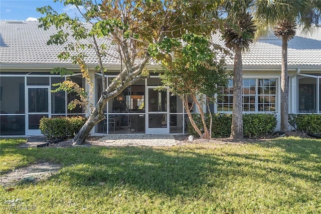 back of property with stucco siding, a lawn, a tile roof, and a sunroom