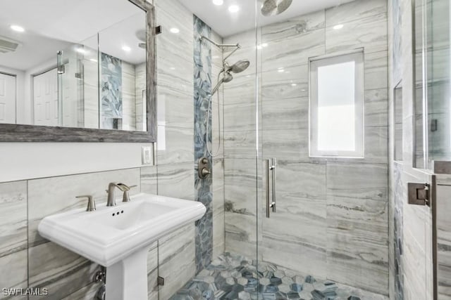 full bathroom featuring a marble finish shower, tile walls, and a sink