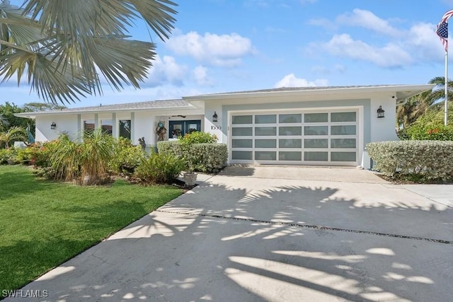 view of front facade featuring a front yard, concrete driveway, an attached garage, and stucco siding