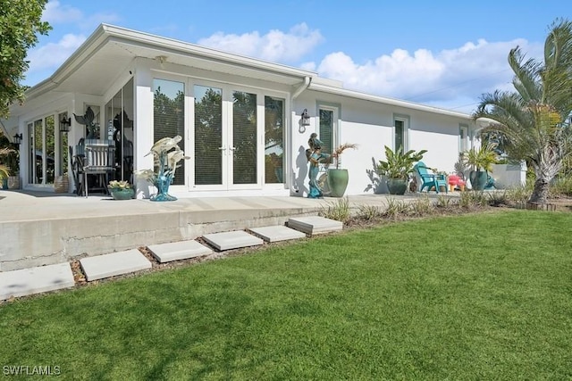 back of house with stucco siding, a lawn, and french doors