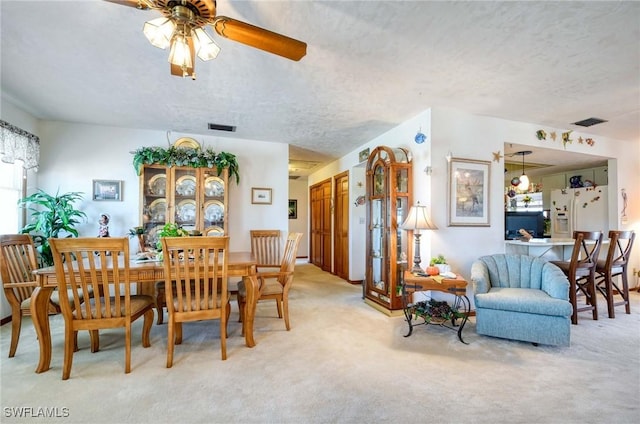 dining room featuring light carpet, ceiling fan, and a textured ceiling