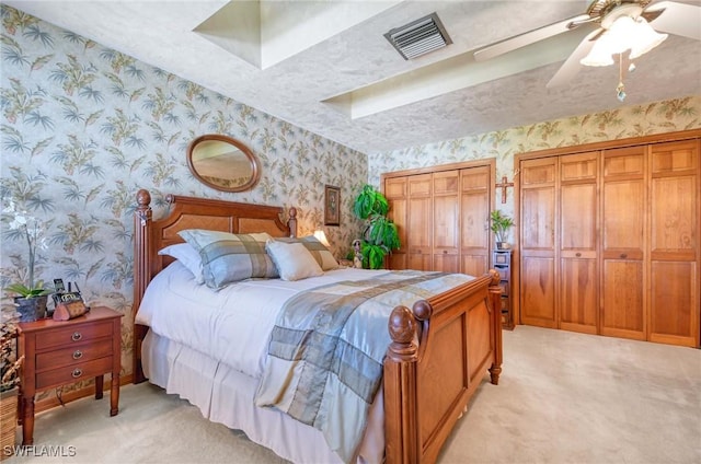 bedroom with ceiling fan, light carpet, and multiple closets