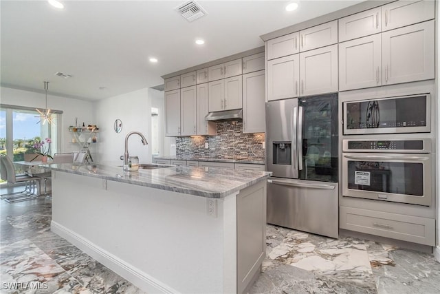 kitchen featuring light stone countertops, sink, stainless steel appliances, gray cabinets, and a kitchen island with sink