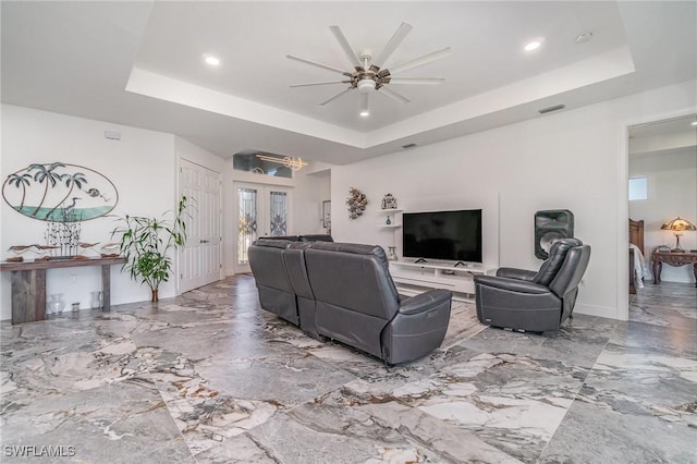 living room with french doors, ceiling fan with notable chandelier, a raised ceiling, and plenty of natural light