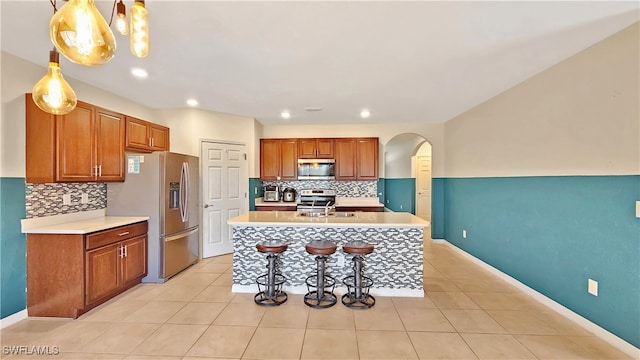 kitchen with pendant lighting, light tile patterned flooring, stainless steel appliances, and a center island with sink