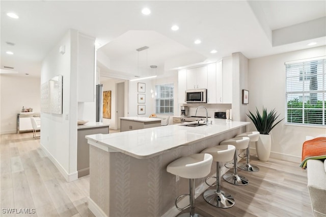 kitchen with kitchen peninsula, light wood-type flooring, sink, white cabinets, and hanging light fixtures