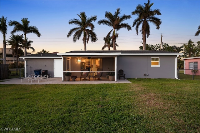 back house at dusk with a patio, a lawn, and a sunroom