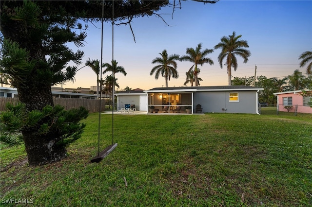 back house at dusk with a lawn and a sunroom