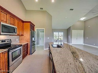 kitchen with appliances with stainless steel finishes, tasteful backsplash, light stone counters, sink, and high vaulted ceiling