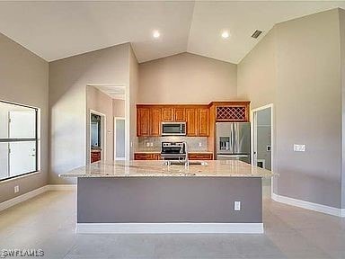 kitchen featuring high vaulted ceiling, a center island with sink, appliances with stainless steel finishes, tasteful backsplash, and light stone counters