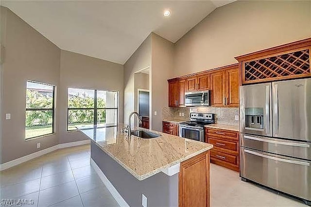 kitchen featuring high vaulted ceiling, a center island with sink, sink, appliances with stainless steel finishes, and light stone counters