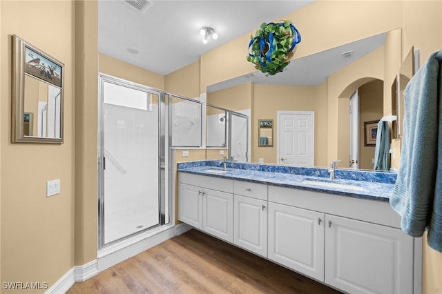 full bathroom with a shower stall, wood finished floors, double vanity, and a sink