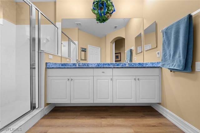 full bathroom featuring double vanity, a shower stall, baseboards, and wood finished floors