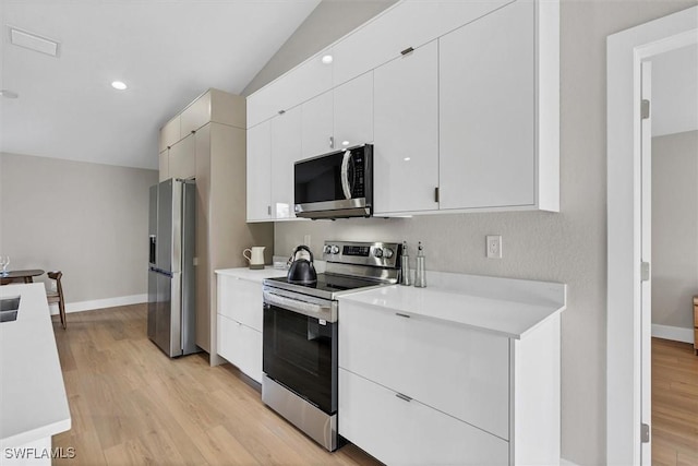 kitchen featuring stainless steel appliances, light hardwood / wood-style flooring, white cabinetry, and lofted ceiling