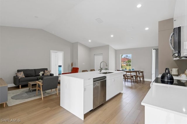 kitchen with stainless steel appliances, vaulted ceiling, sink, light hardwood / wood-style flooring, and an island with sink