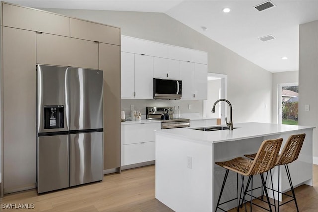 kitchen with appliances with stainless steel finishes, vaulted ceiling, sink, a center island with sink, and light hardwood / wood-style floors