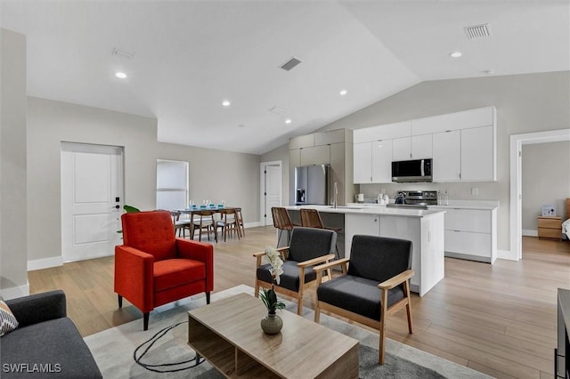 living room with light hardwood / wood-style floors, vaulted ceiling, and sink