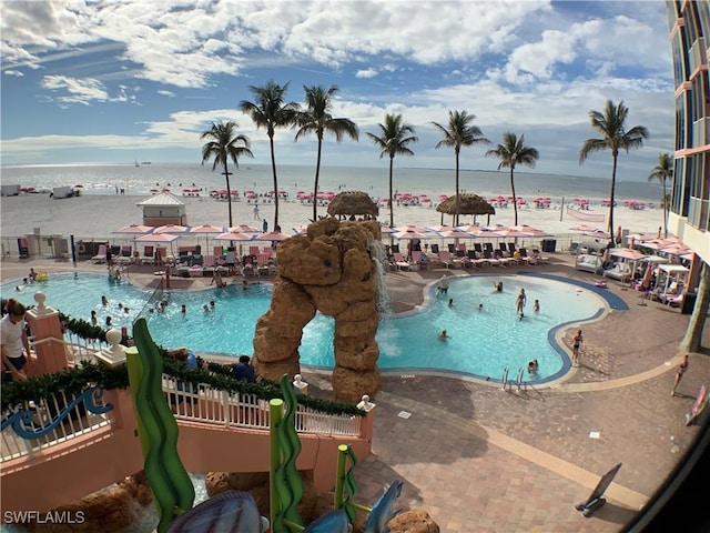 view of swimming pool featuring a water view, a patio, and a beach view