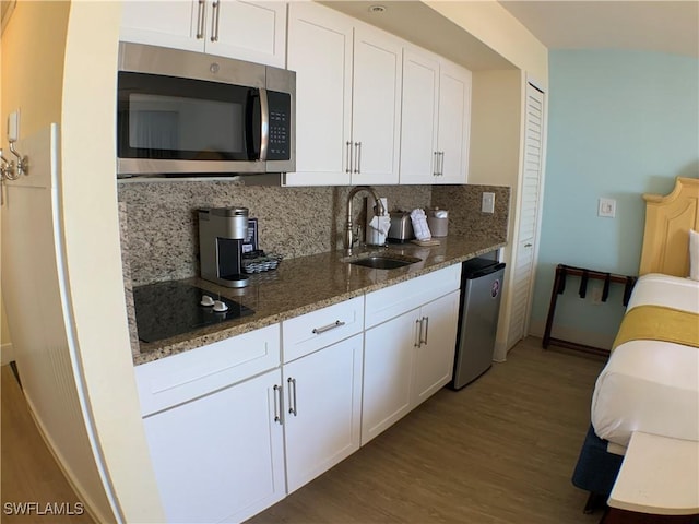 kitchen featuring light wood-type flooring, stainless steel appliances, sink, dark stone countertops, and white cabinets