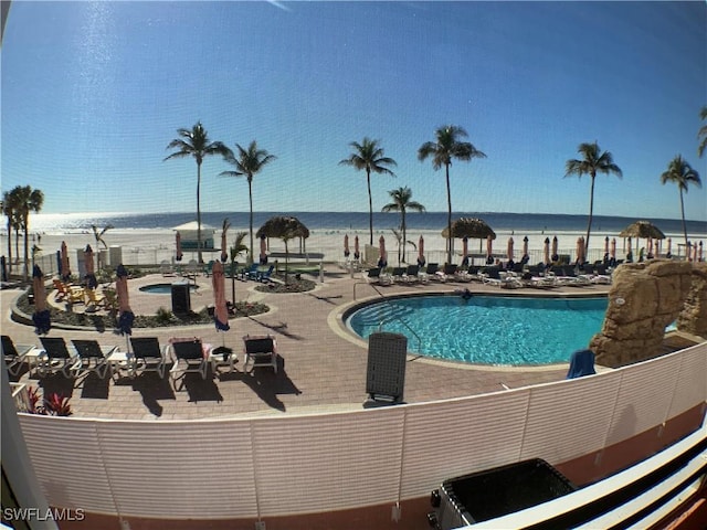 view of swimming pool featuring a patio area, a water view, and a view of the beach