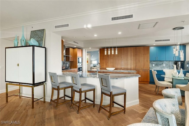 kitchen with kitchen peninsula, decorative light fixtures, tasteful backsplash, and light hardwood / wood-style flooring