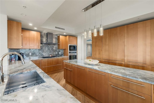 kitchen featuring appliances with stainless steel finishes, light stone counters, sink, wall chimney range hood, and light hardwood / wood-style flooring