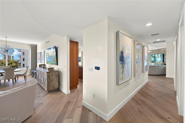 hallway with light hardwood / wood-style flooring and an inviting chandelier