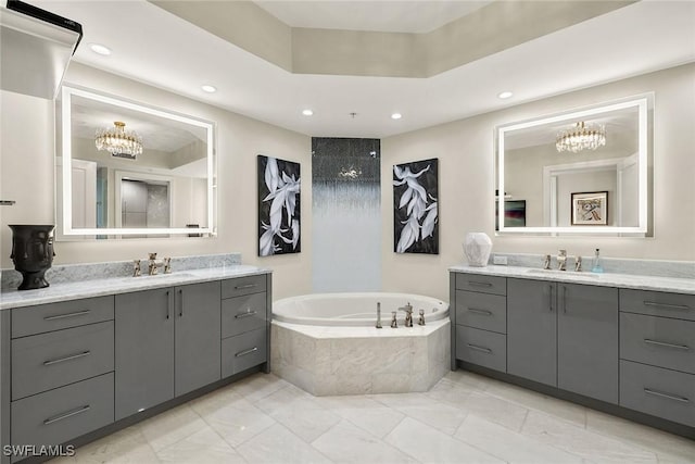 bathroom featuring a chandelier, vanity, and a relaxing tiled tub