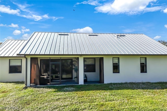 back of house featuring metal roof, a sunroom, a yard, stucco siding, and a standing seam roof