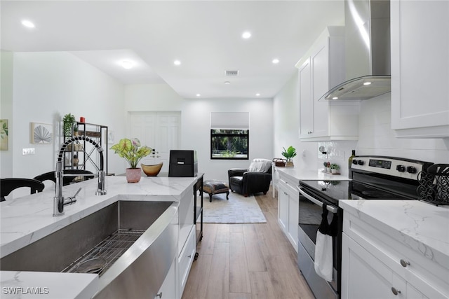 kitchen with stainless steel electric range oven, wall chimney range hood, white cabinets, and light stone countertops