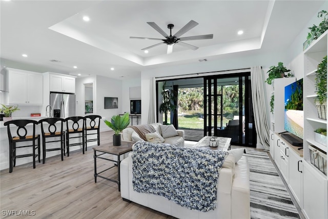 living area featuring light wood-style flooring, a raised ceiling, a ceiling fan, and recessed lighting