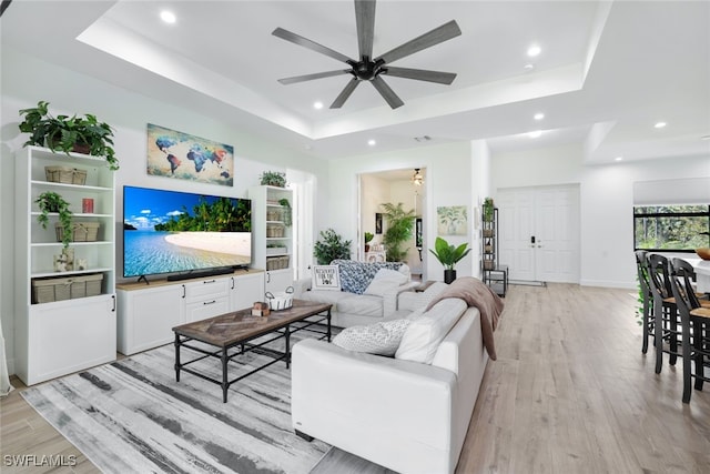 living room featuring light wood finished floors, a tray ceiling, and recessed lighting