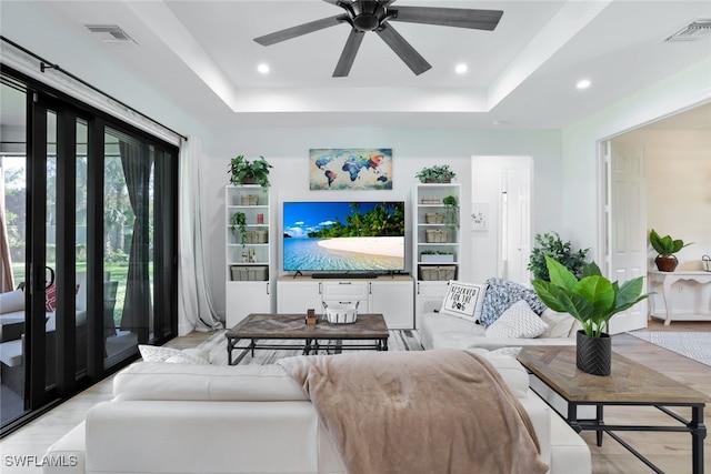 living room with a tray ceiling, visible vents, and recessed lighting