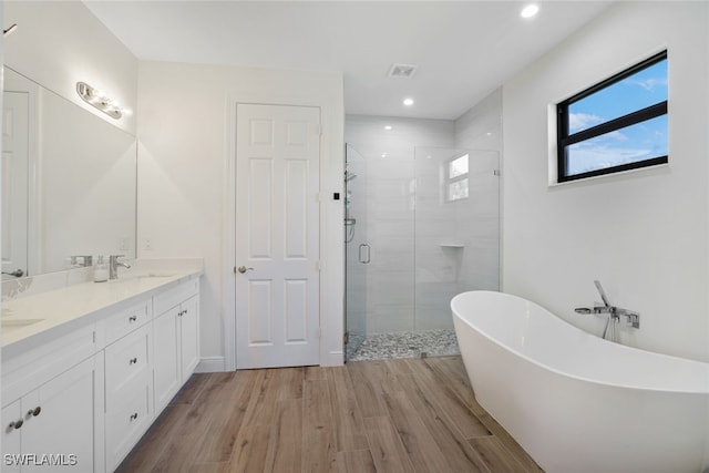 full bath featuring double vanity, a sink, a shower stall, wood finished floors, and a freestanding tub