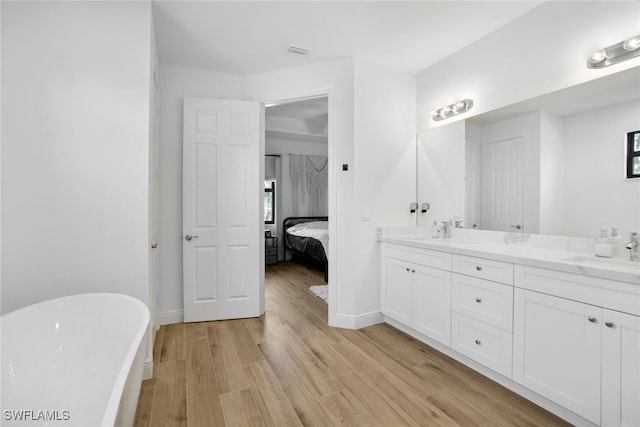 ensuite bathroom with double vanity, visible vents, wood finished floors, a freestanding bath, and a sink